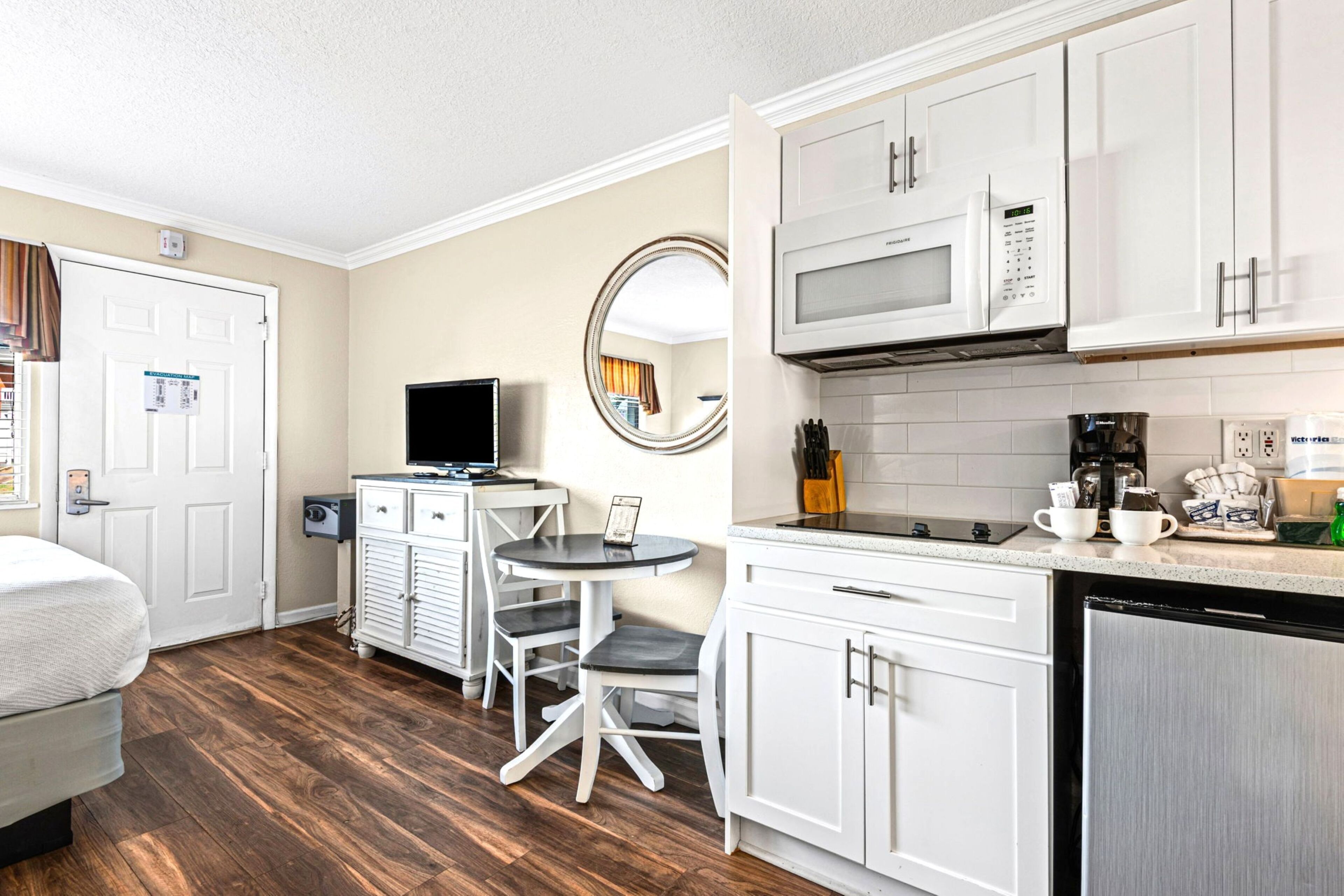 A compact hotel room with a bed, a small dining table with chairs, a television, a microwave, and a refrigerator.