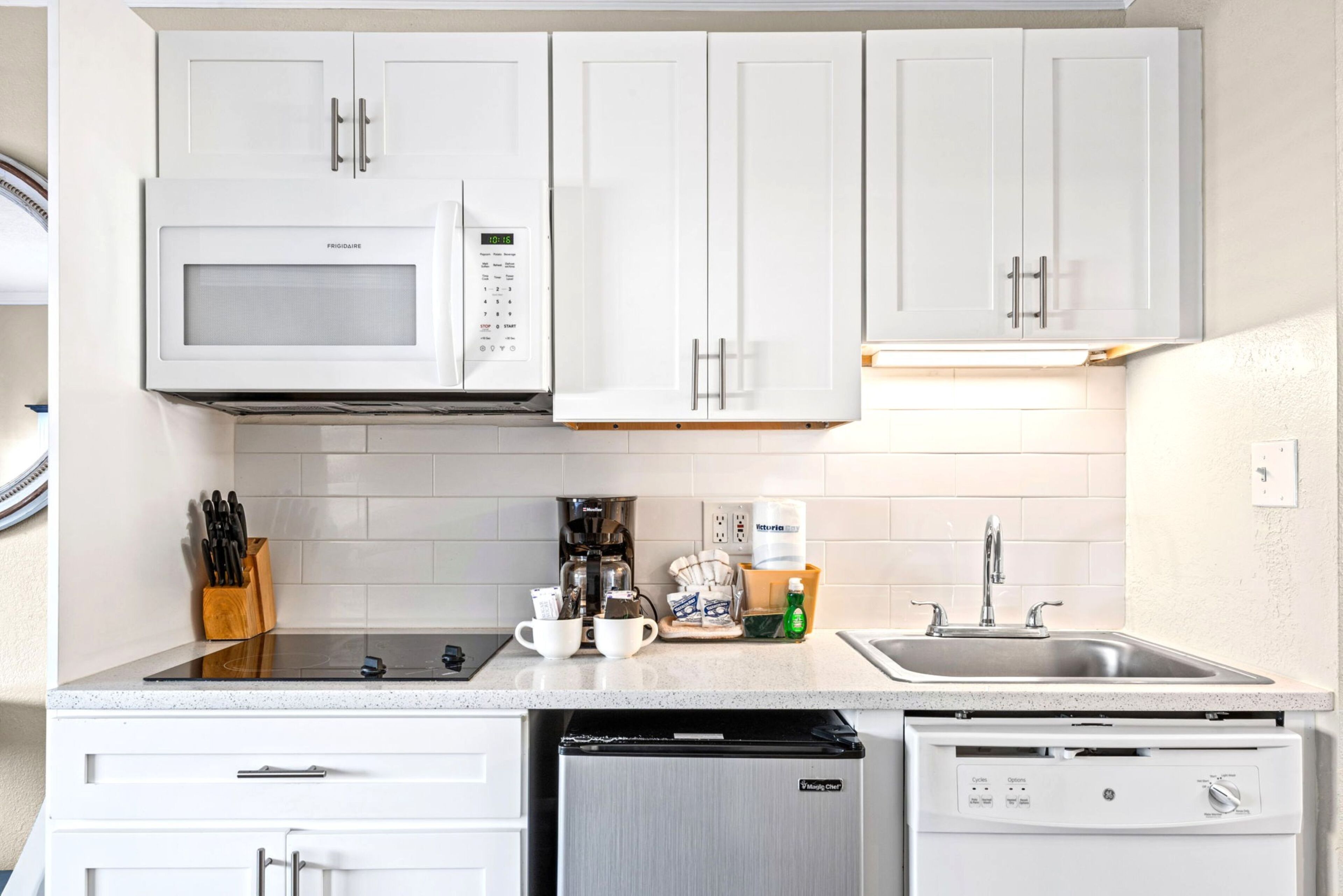 A modern kitchen with white cabinets, a built-in microwave, a coffee maker, and a dishwasher.