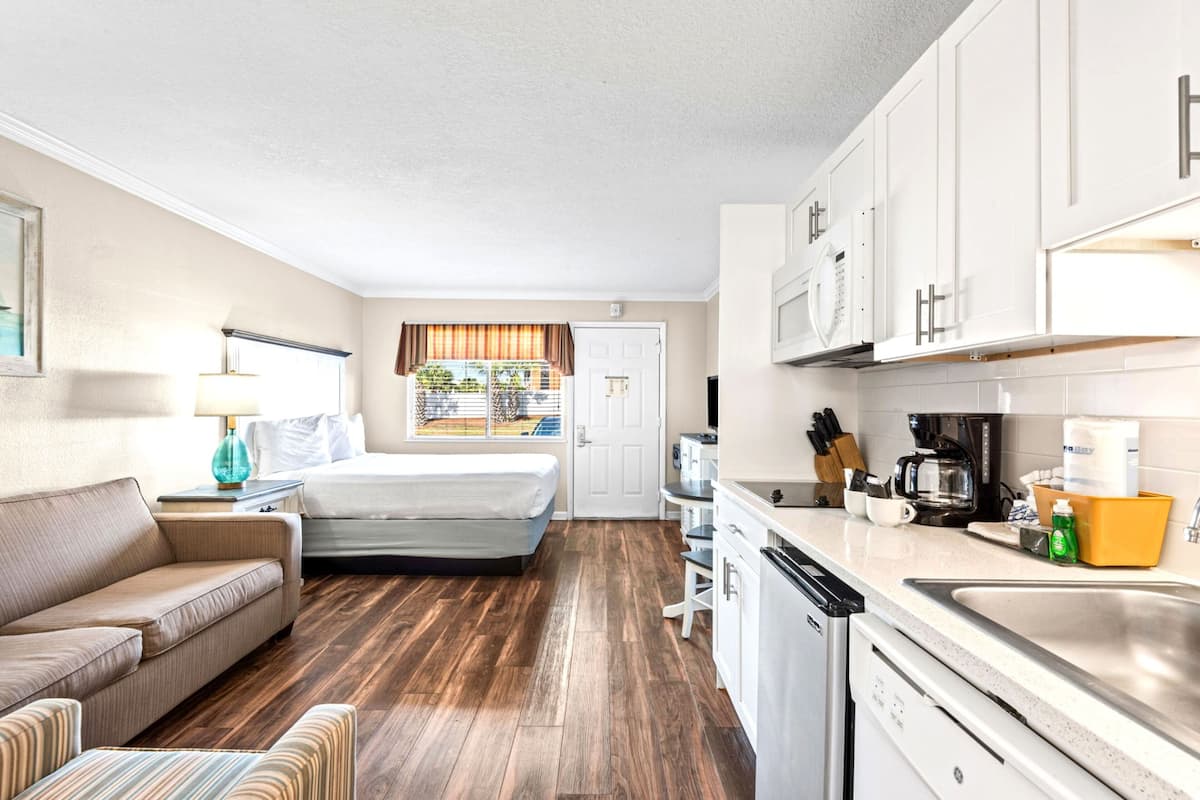 A compact room with a bed, a sofa, a kitchenette, and a window with curtains.