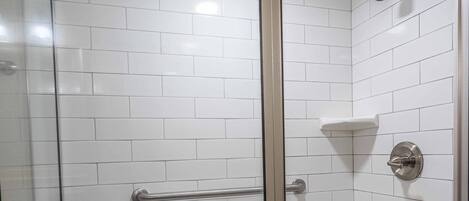 Ducha con paredes de azulejos blancos y barra de apoyo metálica, completamente cerrada con vidrio.