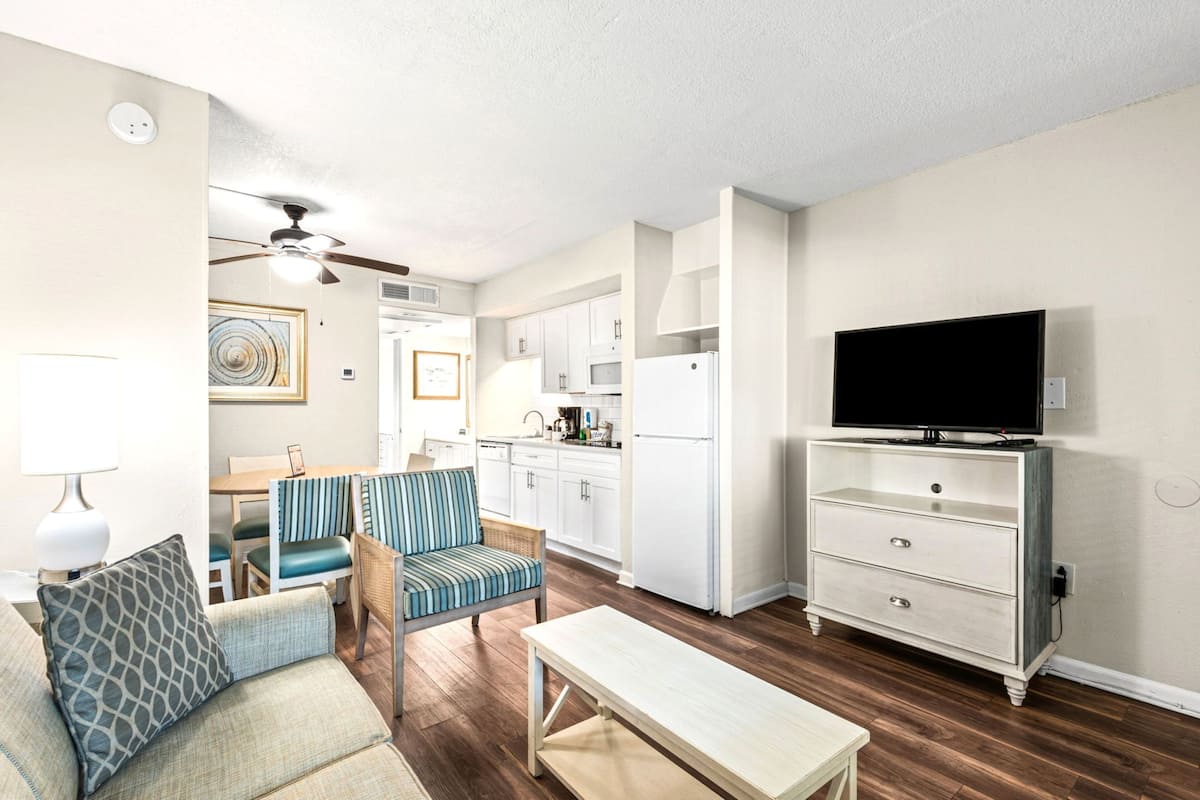 A compact living space with a kitchenette, a dining area, a TV, and a seating area with a sofa and chairs.