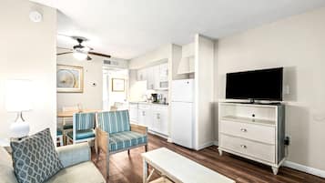 Un espacio habitable compacto con kitchenette, comedor, televisor y zona de estar con sofá y sillas.