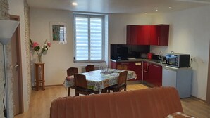 Una cocina compacta con armarios rojos, una mesa de comedor con sillas y una ventana con persianas.