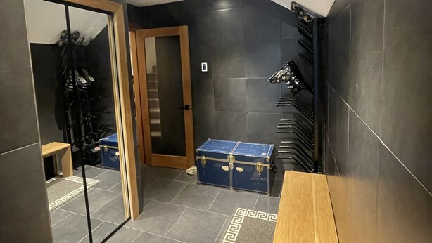 Un baño moderno con baldosas oscuras, un banco de madera, un cofre azul y un tragaluz.