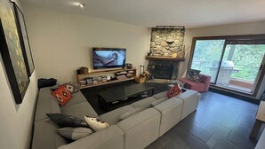 Una sala de estar moderna con un sofá modular grande, un televisor de pantalla plana, una chimenea de piedra y un balcón con una parrilla.