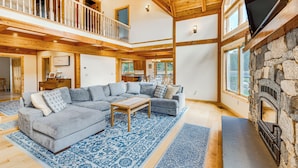 Ein geräumiges Wohnzimmer mit einem großen Ecksofa, einem Holztisch und einem Kamin aus Stein.