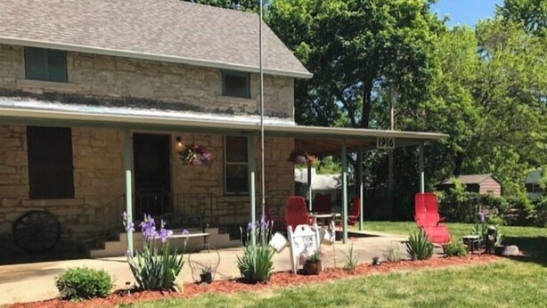 A stone house with a covered porch, numbered 1916, featuring red chairs and purple flowers. - The Strong Inn, Step back in time.  (Manhattan)