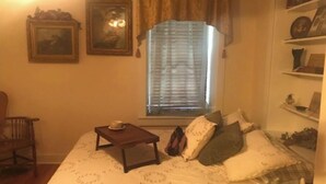 A bedroom with a bed, a small table with a cup, a chair, a window with blinds, and wall-mounted shelves with items. - The Strong Inn, Step back in time.  (Manhattan)