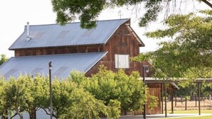 A rustic barn with a metal roof and wooden walls, surrounded by trees and a covered area. - Country house with Pond and EV charger (Exeter)