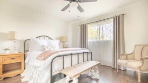 A bedroom with a bed, bedside tables, a bench, a chair, and a ceiling fan. - Country house with Pond and EV charger (Exeter)