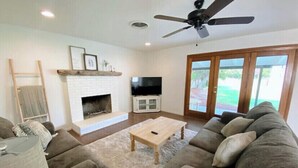 A living room with a fireplace, a ceiling fan, a television, and a large window. - Country house with Pond and EV charger (Exeter)