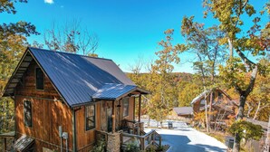 A rustic cabin with a metal roof, wooden walls, and a stone foundation. It features a porch with a railing and a small staircase leading to the entrance. - Adorable Cabin Near PF/Island Hottub GameRoom 2Bed Sleeps 5 Air Hockey Private (Pigeon Forge)