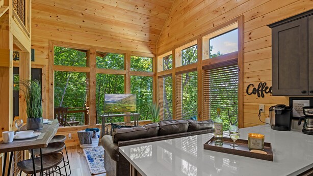 A cozy cabin interior with a large wooden dining table, a comfortable sofa, and a kitchen area with a coffee station. - Adorable Cabin Near PF/Island Hottub GameRoom 2Bed Sleeps 5 Air Hockey Private (Pigeon Forge)