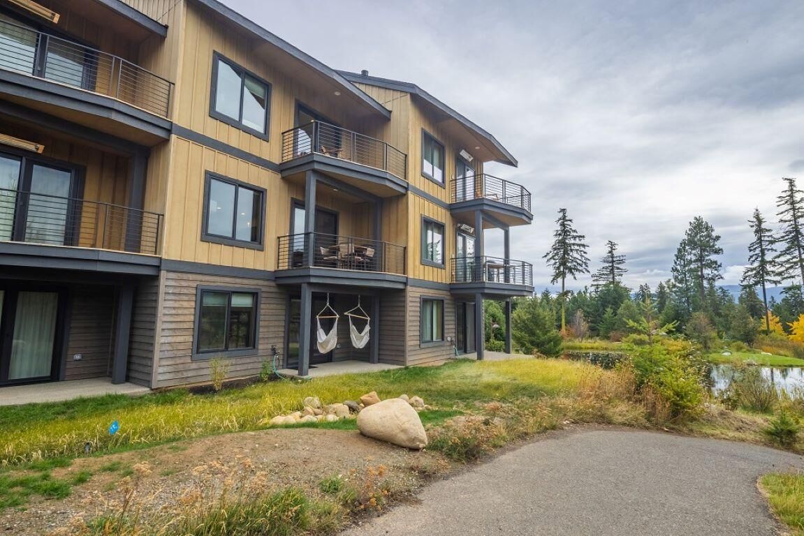 Un immeuble à plusieurs étages doté de balcons, de grandes fenêtres et offrant une vue sur un lac et des arbres.