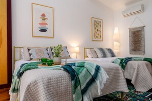 A bedroom with two beds, a bedside table with a plant and a tray, and wall art. - New Park Event Venue & Suites (Ithaca)