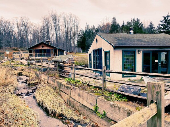 A rustic cabin with a wooden deck and a small stream running beside it. - New Park Event Venue & Suites (Ithaca)