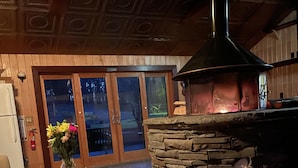 A stone fireplace with a chimney, a wooden table with a vase of flowers, and a door leading outside. - New Park Event Venue & Suites (Ithaca)