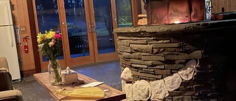 A stone fireplace with a chimney, a wooden table with a vase of flowers, and a door leading outside.