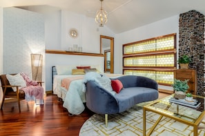 A modern living room with a bed, a blue sofa, a glass coffee table, and a stone accent wall. - New Park Event Venue & Suites (Ithaca)