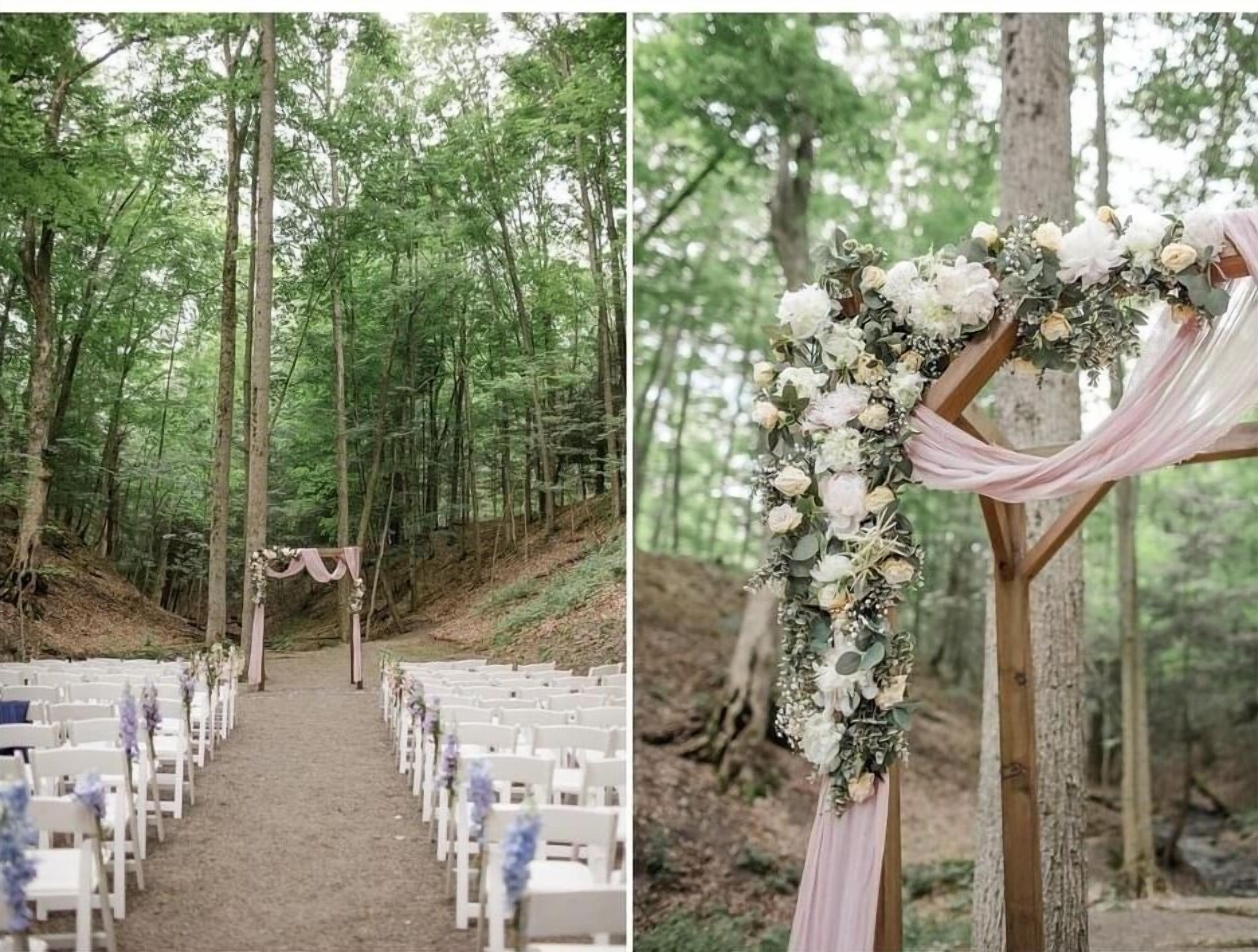A forested venue with a dirt aisle leading to white chairs arranged in rows, suggesting an outdoor event or ceremony.