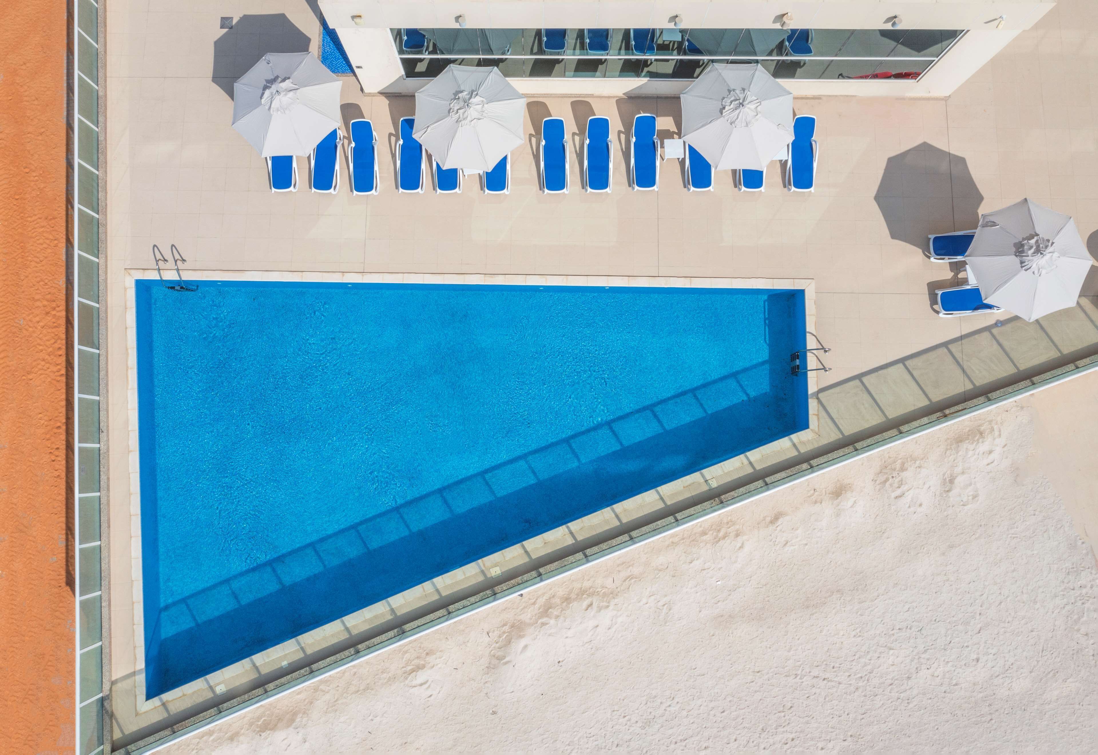 Vista aérea de una piscina con agua azul, rodeada de sillas de descanso y sombrillas.