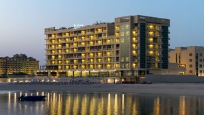 A multi-story hotel with a poolside area and beach chairs. - Radisson Resort Ras Al Khaimah Marjan Island (Ras Al Khaimah)
