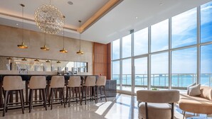 A modern bar area with a high ceiling, large windows, and a view of the sea. - Radisson Resort Ras Al Khaimah Marjan Island (Ras Al Khaimah)