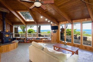 Una sala de estar acogedora con chimenea, sofá y ventanas amplias con vistas al océano.