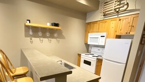 A compact kitchen with wooden cabinets, a built-in island, a microwave, a stove, and a refrigerator. - Getaway to the Mountains (Vernon)