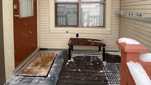 A covered porch with a wooden bench, a door with a number, and a window with blinds. - Getaway to the Mountains (Vernon)