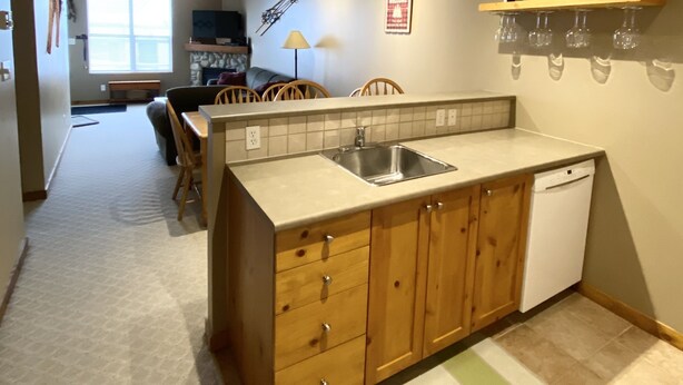 A compact kitchen with wooden cabinets, a built-in dishwasher, and a window providing natural light. - Getaway to the Mountains (Vernon)