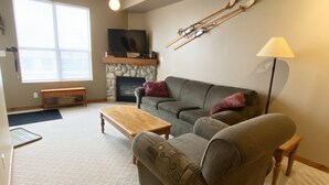 A living room with a sofa, a coffee table, a fireplace, and a television. - Getaway to the Mountains (Vernon)