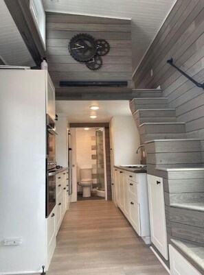 Stylish hallway leads to a compact bathroom with modern cabinetry and dark paneling.