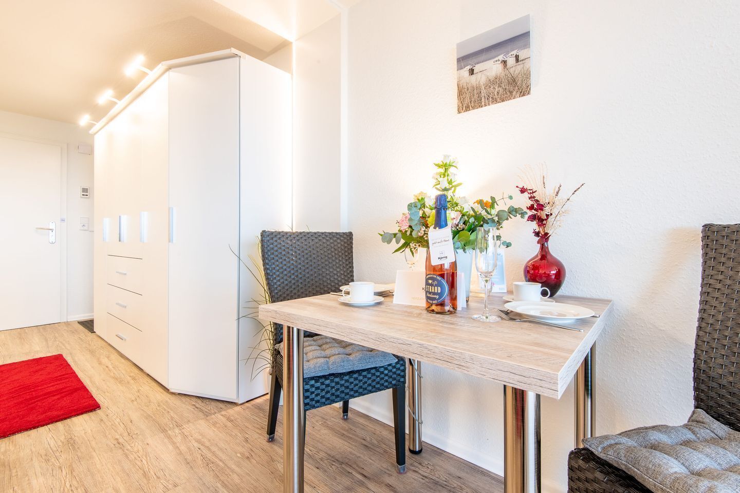 Una habitación de hotel moderna con un área de comedor que incluye una mesa de madera, sillas y un tapete rojo.