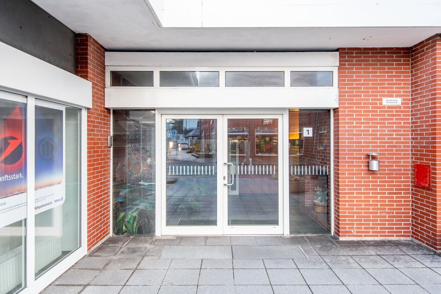 Ingresso di un edificio con porta in vetro, facciata in mattoni e insegna che indica un'attività commerciale o un'area di servizio.