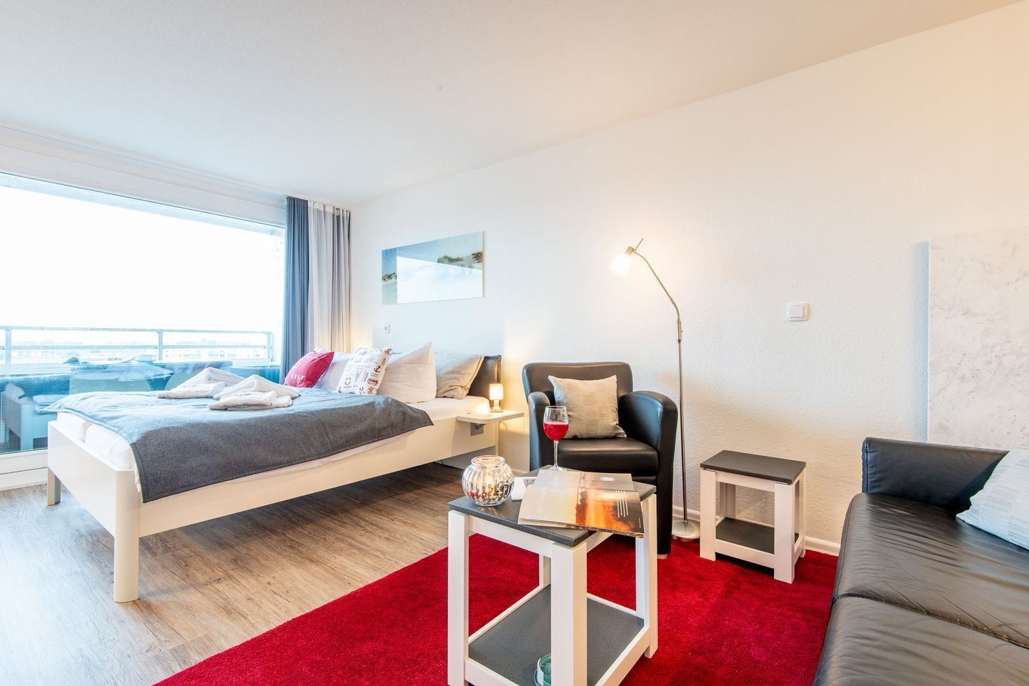 Una habitación de hotel moderna con una cama, un sofá, una mesita, una lámpara de pie y vistas al mar.
