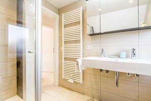 Een moderne badkamer met een douchecabine van glas, een witte wastafel met spiegel en een handdoekrek.