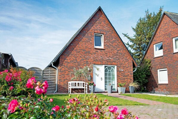 Een huis met rode bakstenen, een puntig dak, een witte deur en het nummer '13' op de muur.