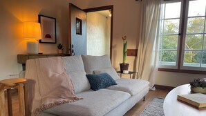 Un salon confortable avec un canapé, une petite table, une lampe et une fenêtre avec des rideaux.
