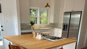 Une cuisine moderne dotée d’un îlot central, de chaises en bois, d’un réfrigérateur en acier inoxydable et de meubles de cuisine blancs.