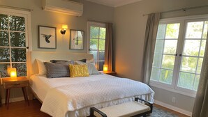 Une chambre à coucher avec un grand lit, des tables de chevet, un banc et de nombreuses fenêtres.