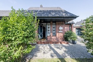 Een bakstenen huis met een donker dak, een voordeur en een kleine tuin met grind en planten.