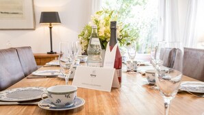 Un tavolo apparecchiato con piatti, bicchieri e una bottiglia di vino, con un cartello di benvenuto e un vaso di fiori sullo sfondo.