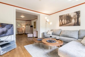 Een moderne woonkamer met een grijze bank, een houten salontafel, een televisie en een schilderij van bomen.