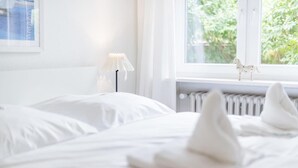 Una camera d'albergo con un letto, un termosifone, una finestra che si affaccia sul verde e un piccolo oggetto decorativo sul davanzale.