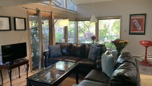 A living room with a sectional sofa, a glass coffee table, a TV on a wooden stand, and a red floor lamp.
