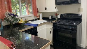A kitchen with white cabinets, a black stove, a microwave, and a window with red curtains.