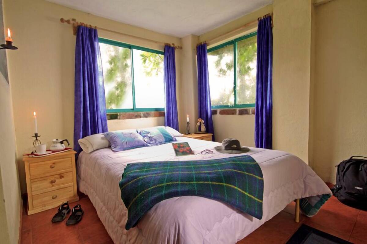A neatly arranged bedroom with a bed, a nightstand, a lamp, and a window with curtains.