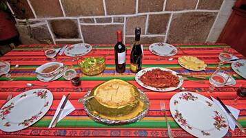 Una mesa dispuesta con platos, cubiertos y una botella de vino, con un mantel colorido y una pared de piedra al fondo.