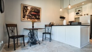 A kitchen with a central island, two chairs, a table with a vase, and a framed picture on the wall.